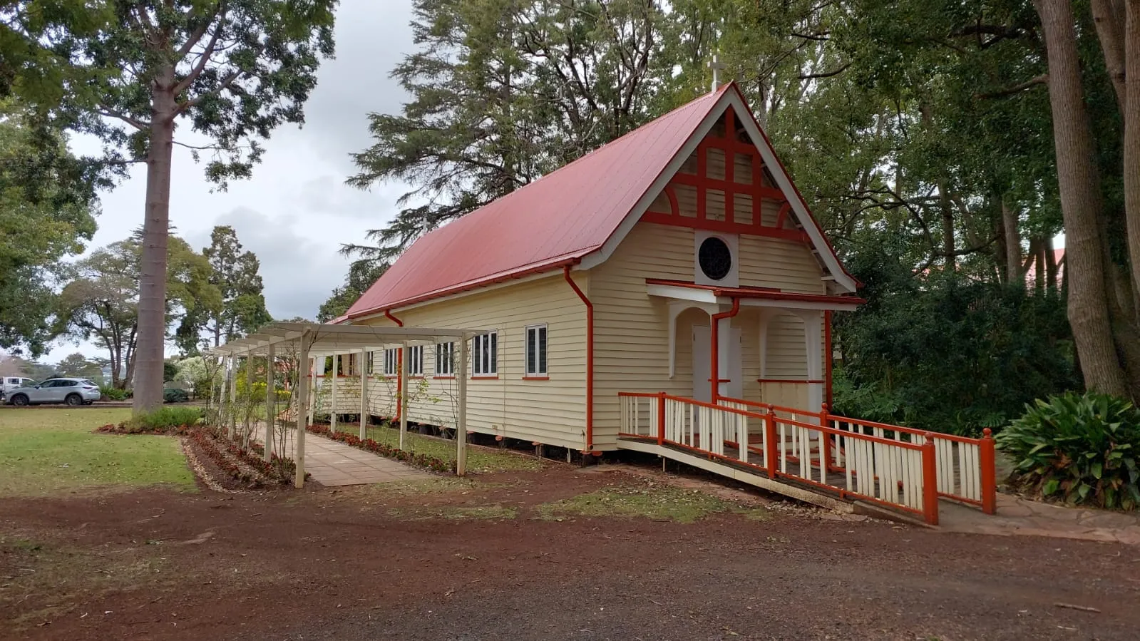 Cream timber heritage chapel with a red gabled roof and access ramp