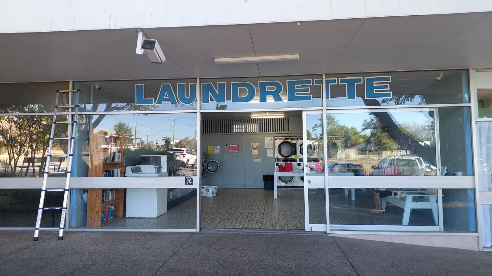 Glass-fronted self-service laundrette with a ladder set up for testing