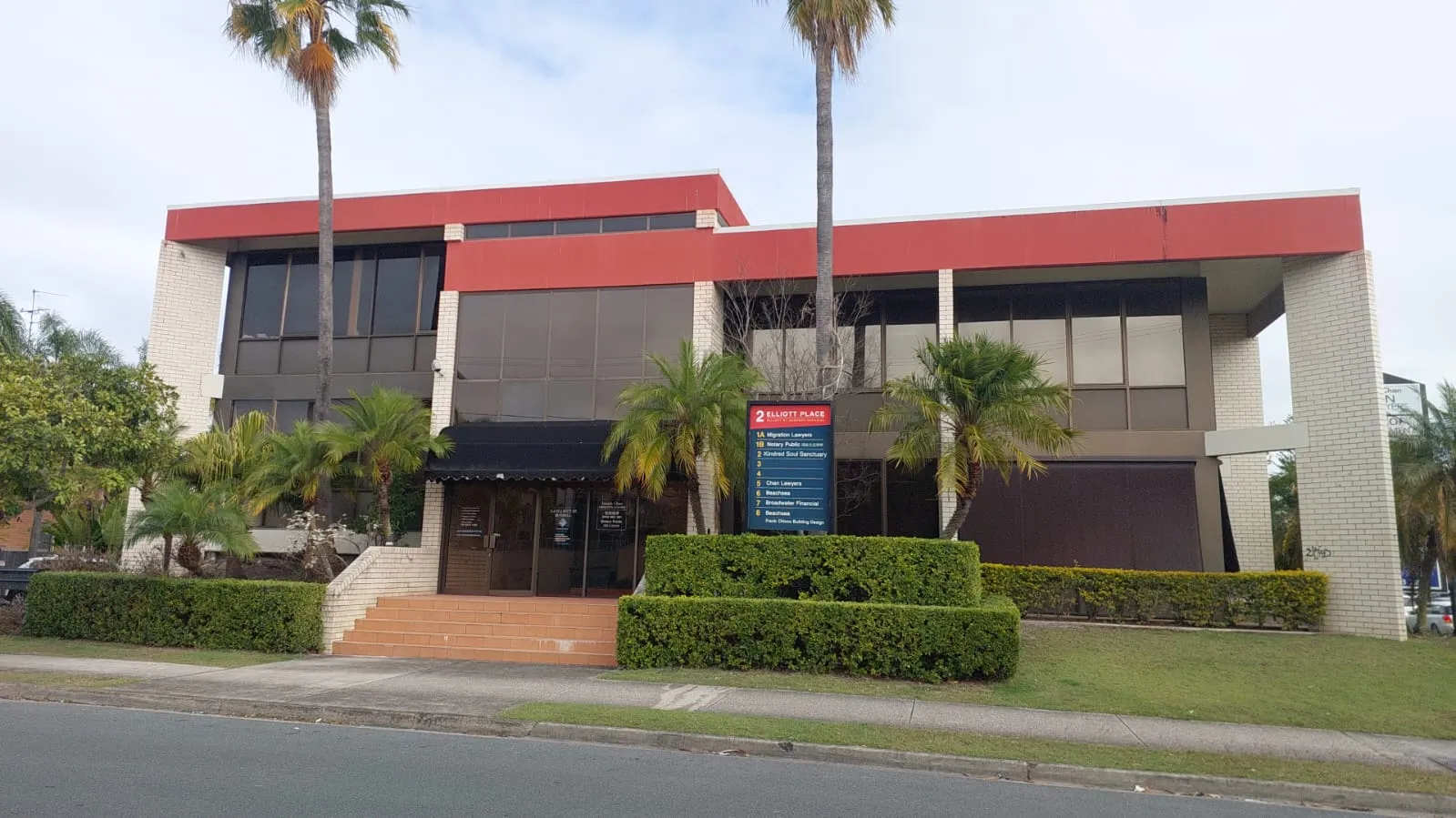 Two-storey commercial office block with red parapet and tenant directory sign