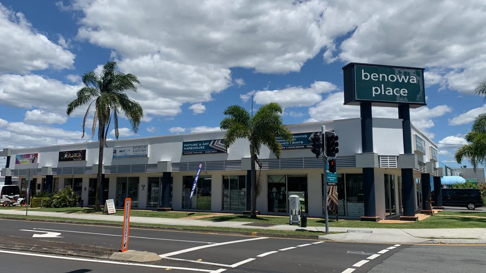 Single-storey retail and showroom strip with a Benowa Place pylon sign