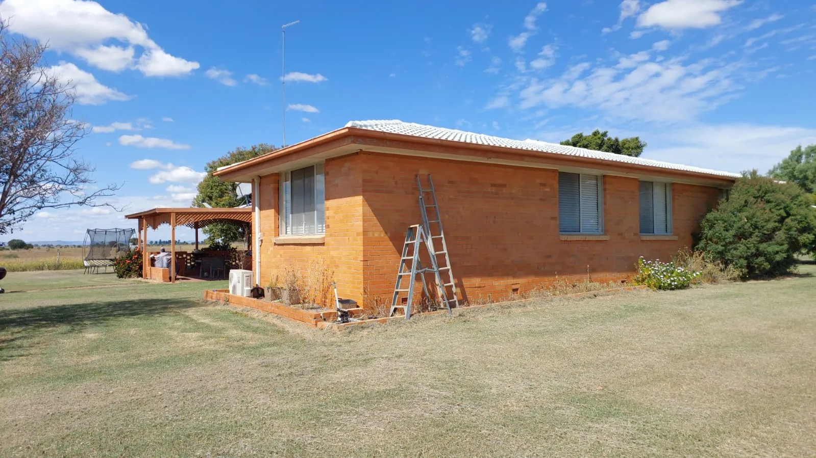 Single-storey brick rural home with a ladder set up against the wall during testing