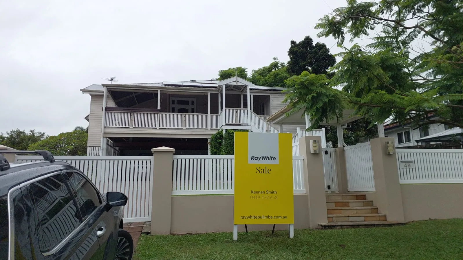 Renovated Queenslander home behind a white fence with a real-estate sale sign