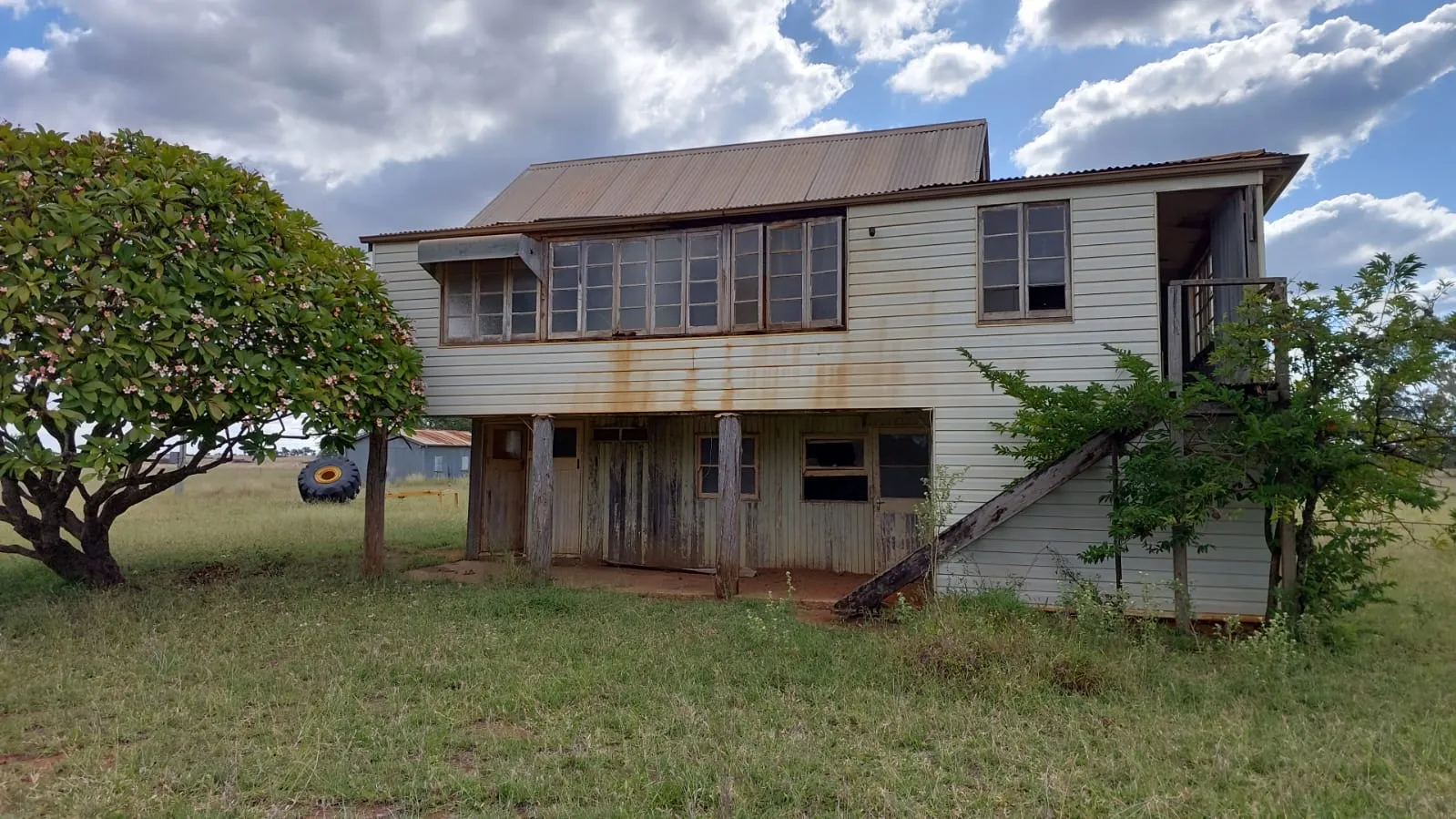 Old weatherboard two-storey Queenslander home on stumps in a rural paddock