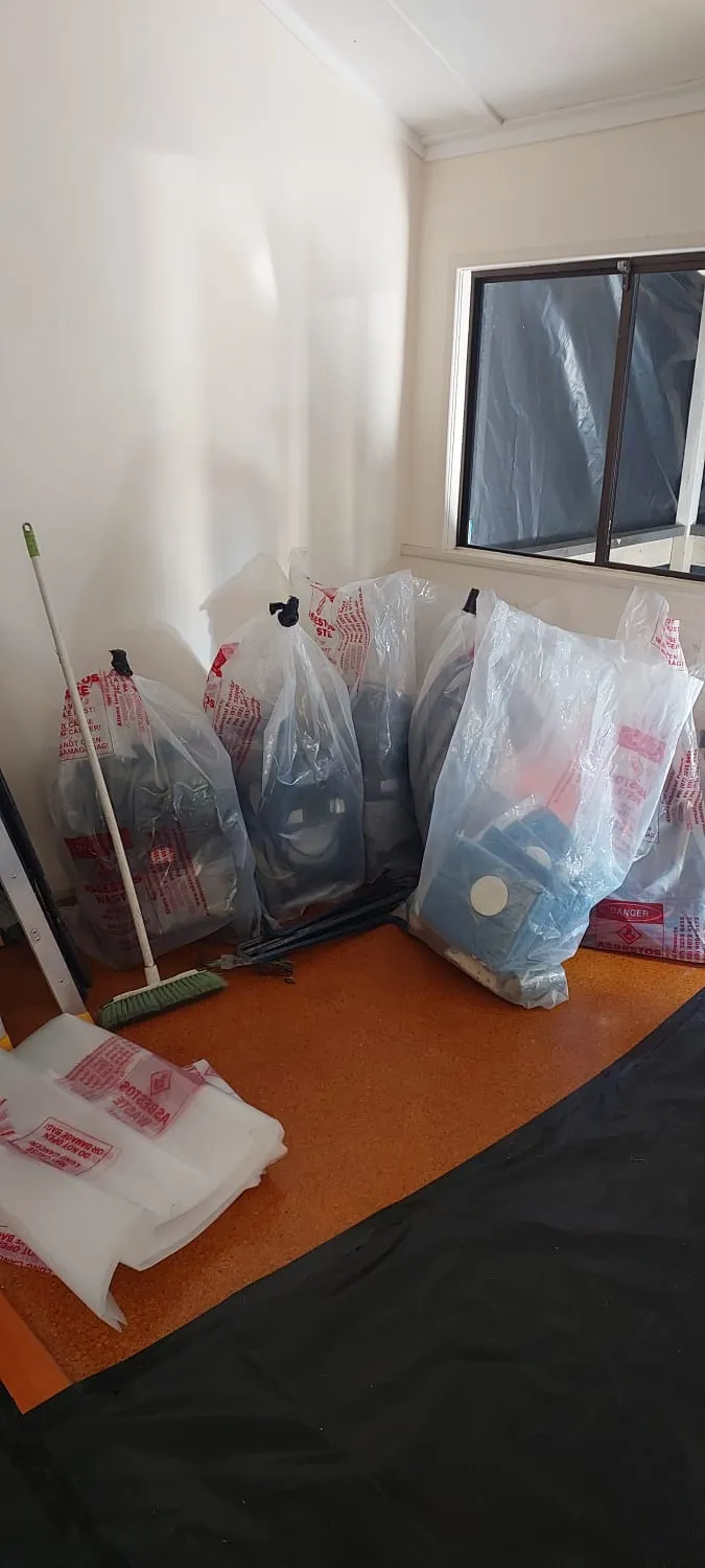 Asbestos waste double-bagged and labelled inside a room prepared for removal