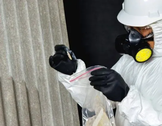 Asbestos Watch technician in PPE bagging a sample on-site